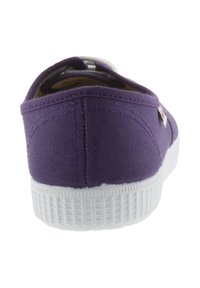 Chaussure en toile violette avec une semelle en caoutchouc blanc. L'arrière présente une texture lisse et une couture, avec une petite étiquette sur le côté.