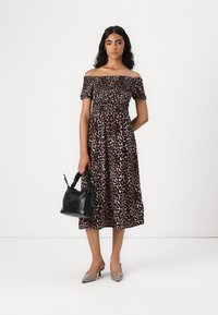 Off-shoulder leopardmönstrad klänning med elastisk midja, knälång, tillsammans med en svart texturerad handväska och beige spetsiga klackar.