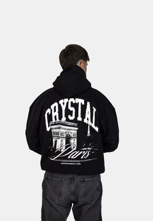 Felpa nera con cappuccio caratterizzata da una grande stampa grafica sul retro, che mostra l'Arc de Triomphe e la Torre Eiffel, con il testo "CRYSTAL Paris".