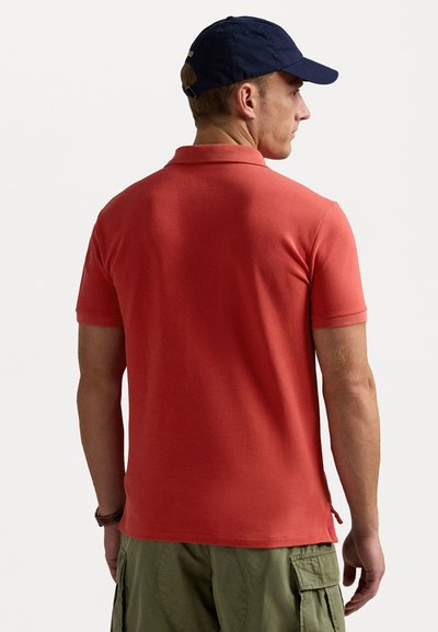Kortärmad, korallfärgad polotröja i bomullstyg. Har en klassisk krage, sidoflikar och en mjuk textur. Bärs med olivfärgade cargo-shorts.