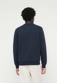 Marineblå genser med rund hals og ribbede mansjetter, med en jevn tekstur og ensfarget design. Logodetalj ved sømmen.