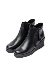 Black ankle boots made of smooth leather with a wedge heel and zipper detail. Features a textured sole and tassel accent.