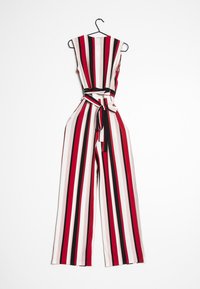 Combinaison rayée avec jambes larges, présentant des rayures verticales rouges, noires et blanches, une ceinture à la taille ajustée et un design sans manches.