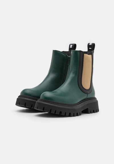 Botas Chelsea de couro verde com sola grossa preta, painéis laterais bege e banda elástica preta. Fecho com ziper no lado interno.