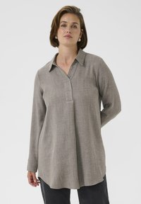 Camicia tunica grigia a maniche lunghe in tessuto testurizzato. Presenta un colletto, una patta frontale e un orlo curvo. Abbinate a pantaloni scuri.