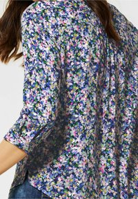 Kukkakuosiset puserot, joissa on sinisiä, vaaleanpunaisia ja vihreitä kuvioita. Kevyt kangas, pitkät hihat nappidetaljalla, rento malli ja sivuaukot.