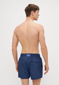 Marineblaue Badeshorts mit elastischem Bund, Gesäßtasche und Logopatch. Glatte Textur, knielange Länge und moderne Passform.