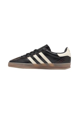 Sneaker nera low-top con strisce bianche, suola in gomma e linguetta sul tallone color crema mostrata di profilo laterale.