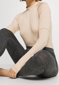Ljusbeige långärmad topp med hög krage, parat med mörkgrå leggings med en subtil textur och figurnära design.