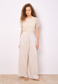 Top de ganchillo beige con mangas cortas, combinado con pantalones de lino ligeros de pierna ancha que tienen cintura elástica y detalle de cordón.