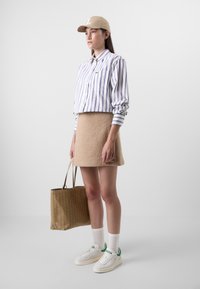 Gestreepte blouse met lange mouwen, beige wollen rok, witte sneakers met groene accenten, beige pet en een beige totebag.
