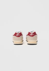Une paire de baskets New Balance beige et grise avec des accents de talon bourgogne, vue de l'arrière sur un fond blanc uni.