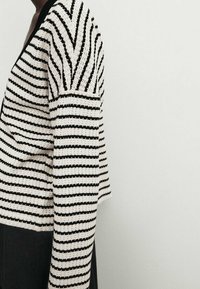 Pull en tricot rayé avec des lignes horizontales noires et blanches, doté de manches longues et d'un décolleté en V, texture tricotée et coupe ample.