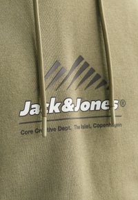 Olive green hoodie with a textured fabric, featuring a large black and white logo. Drawstrings match the fabric color.