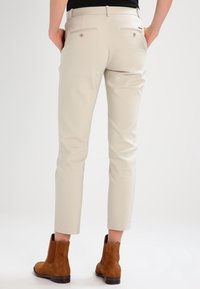 Beige skräddarsydda byxor med bakfickor och smal passform, gjorda av slät tyg, i kombination med bruna ankelstövlar. Enkelt utförande utan synliga mönster.