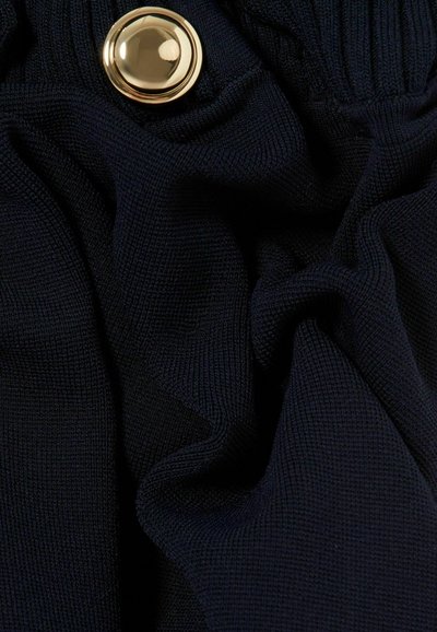 Tissu tricoté bleu marine à la surface légèrement texturée, avec un grand bouton doré sur la taille, mettant en avant un matériau lisse et doux.