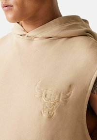 Beige ärmelloses Hoodie mit einem strukturierten, gestickten Bullen-Logo auf der Brust. Weicher Stoff mit lockerer Passform und Kapuze.