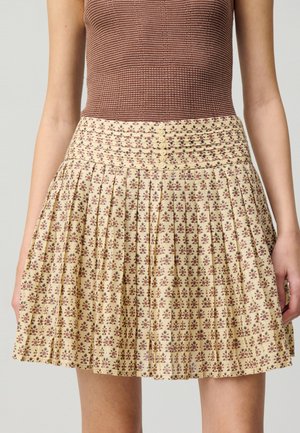 Gonna con motivo floreale in crema con accenti rosso scuro; presenta delle pieghe e una vita arricciata con dettagli di bottoni.