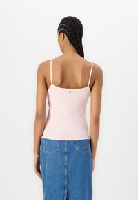 Lyse rosa spaghetti stropp topp med ribbet tekstur, bølgete kanter og en liten logo detalj på baksiden, kombinert med et denimkjørt.