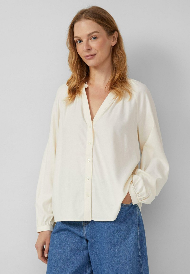 Gebroken witte button-up shirt met een v-hals, lange mouwen en elastische manchetten. Gecombineerd met blauwe denim jeans.