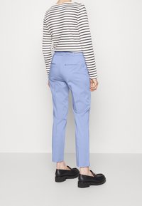 Helle blaue maßgeschneiderte Hose mit glatter Textur, kombiniert mit einem gestreiften Langarmoberteil. Schwarze Loafers runden das Outfit ab. Rückansicht gezeigt.