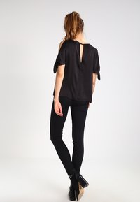 Black silk blouse with short sleeves, open back design, and knot accents at the sleeve hems, paired with black skinny jeans and ankle boots.