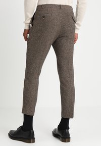 Brown herringbone-patterned trousers with a slim fit, featuring pockets, belt loops, and a smooth texture, paired with black shoes.