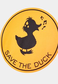 Żółta okrągła łatka z czarnym sylwetką kaczki, z nutkami i napisem "OCAL DUCK" u dołu.