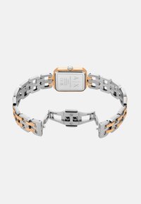 Nerezová oceľ a zlatý hodinkový tón s obdĺžnikovým čelom, prepojeným pásikom a uzáverom. Zadná strana zobrazuje logo značky a podrobnosti.