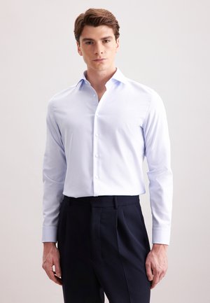 Camicia azzurra chiaro con colletto classico, maniche lunghe e tessuto morbido. Abbinata a pantaloni scuri a vita alta.