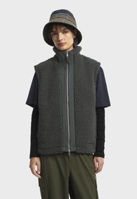 Gilet en polaire gris foncé avec un col haut, une fermeture éclair à l'avant et une texture douce ; porté par-dessus une chemise bleu marine et associé à un pantalon cargo olive.