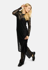 Juoda nėriniuota suknelė su ilgomis rankovėmis, puošta gėlių raštu ir šoniniu įkirpimu. Derinama su derančiomis nėriniuotomis kelnėmis ir juodais lygiais bateliais.