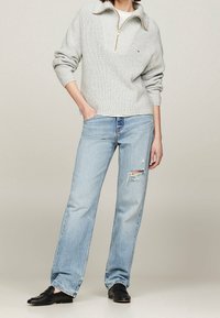 Lys grå strikket pullover med en halv lynlås krave, parret med lyseblå slidte lige jeans og sorte loafers.