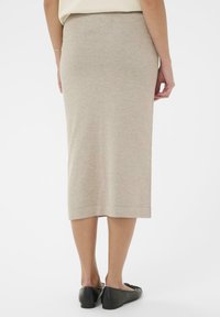 Béžová pletená sukně střední délky s přiléhavým střihem a jemnou texturou. Lem končí těsně nad kotníkem. Kombinováno s černými balerínami na rovné podrážce.