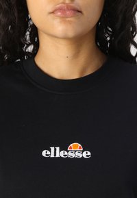 Sort bomulds t-shirt med et hvidt broderet "ellesse" logo og en orange bue ovenover. Udringen har en klassisk rund hals.