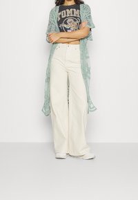 Kimono largo azul claro con un patrón de encaje floral sobre una camiseta gráfica negra con un tigre, combinado con pantalones de pierna ancha blanca de tiro alto.