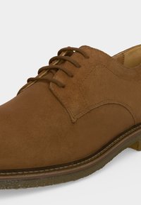 Chaussure à lacets en suède marron avec détails cousus et semelle texturée, vue en gros plan de côté.