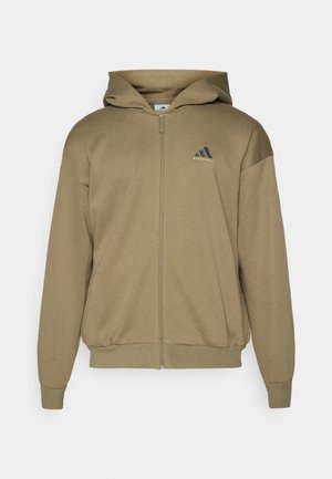 Khaki zip-up hættetrøje lavet af et blødt, struktureret stof. Den har en hætte, ribbede manchetter, en ribbede kant og et sort logo på brystet.