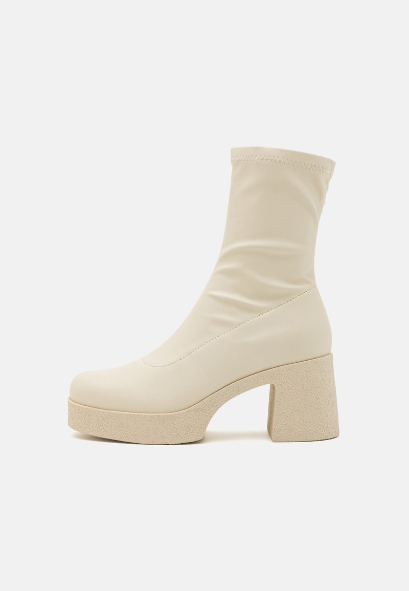 Beige ankelskobror i slätt syntetmaterial, med en kroppsnära silhuett, kraftig texturerad klack och plattformsula.