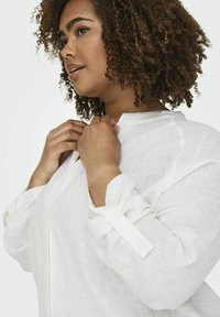 Blusa bianca in lino con colletto, chiusura a bottoni e maniche arrotolate. Tessuto texture con vestibilità morbida.