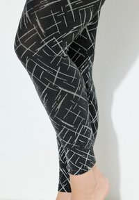 Czarne legginsy z metalicznym, srebrnym wzorem geometrycznym. Wykonane z elastycznego materiału, charakteryzują się gładką fakturą i długością do kostek.