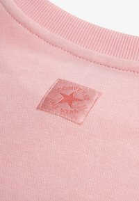 Ροζ ανοιχτό φούτερ με ριμπ λαιμόκοψη και τετράγωνο κεντητό λογότυπο με αστέρι και όνομα μάρκας. Μαλακή υφή.