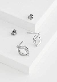Silverfärgade örhängen i bladform med en slät yta, som har en elegant design och bakåtslutande beslag, uppvisade på vita ytor.