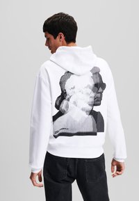 Weißer Kapuzenpullover mit einem schwarzen grafischen Porträt-Design und gerippten Akzenten auf der Rückseite, in lockerer Passform und mit Kängurutasche.