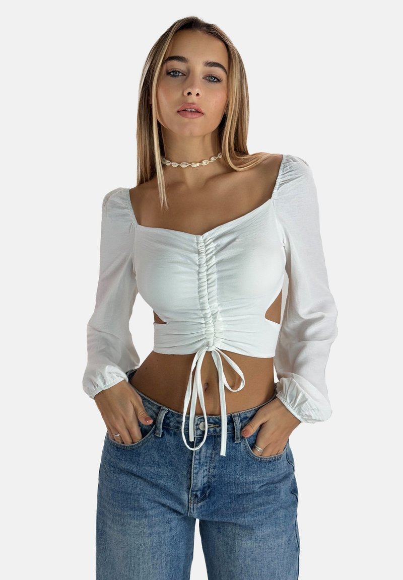 Vit kort top med långa puffärmar, dragsko fram, ruching-detaljer och utskärningar på sidorna, tillsammans med högmidjade blåjeans.