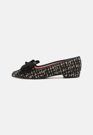 Black and cream tweed flat shoe with a pointed toe, low block heel, and a bow accent on the side. Textured fabric with intricate pattern.
