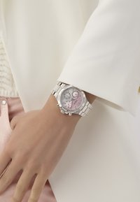 Silver chronograph watch with a pink and gray dial, diamond accents, metal bracelet, and circular case, worn on a hand.