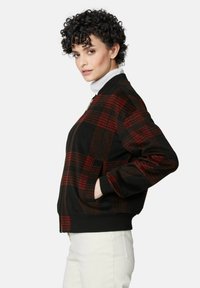 Zwarte bomberjack met een rood en zwart geruit patroon. Voorzien van ribgebreide manchetten en zoom, ritssluiting en zijzakken. Textuurstof.