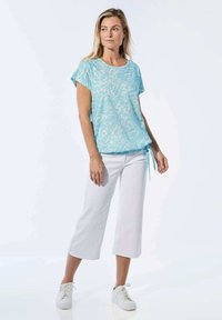 Helles blaues Kurzarmoberteil mit einem strukturierten Muster, kombiniert mit weißen Caprihosen und weißen Turnschuhen, die eine verstellbare Taille besitzen.