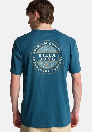 Maglietta in cotone turchese con logo circolare recante la scritta "BILLA BONG" e un motivo tropicale, posizionata in modo ben visibile sulla schiena. Maniche corte.